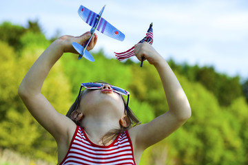 Patriotic girl playing with airplane while holding American flag outside 