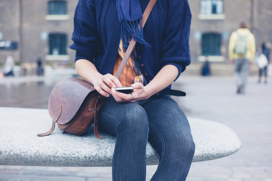 Woman sitting on granite bench using smart phone