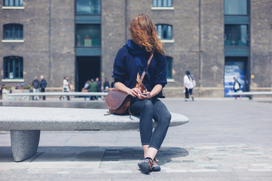 Woman sitting on granite bench using smart phone
