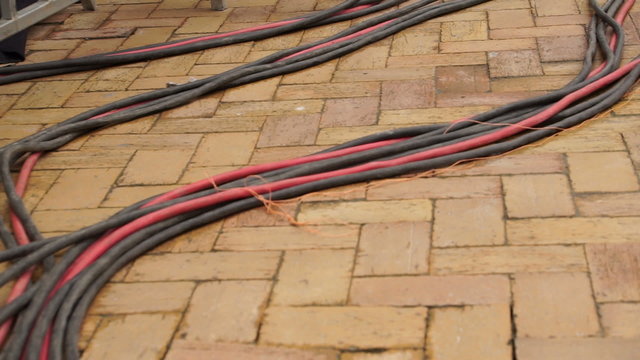 Heavy gauge electrical power cable mains laying on the brick covered ground behind the stage at an outdoor event.