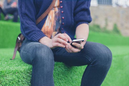 Woman sitting on astro turf using smart phone