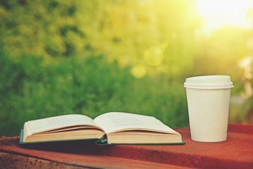 paper cup of coffee and book in the green grass in summer sunlig
