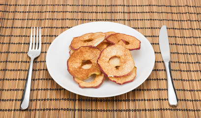 Dried apple slices served on a plate on tablecloth. With cutlery on the sides.