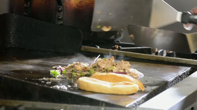 A chef adding a bun to the grill to be toasted
