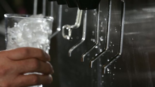 Close up of a glass being filled with ice and cola at a soda fountain

