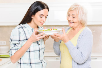 Obraz na płótnie Canvas Granddaughter smelling salad in kitchen