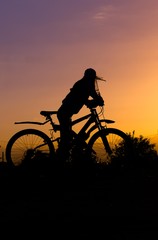 Obraz premium Silhouette of a gerl with a bicycle against the sky at sunset,