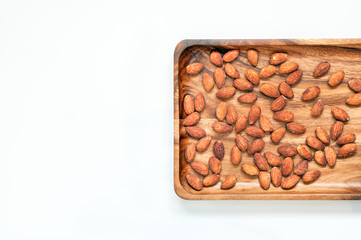 Salted & roasted almonds on wooden saucer and white background