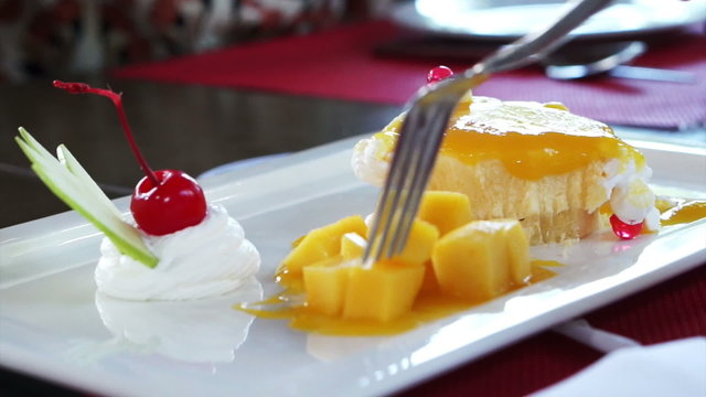 Eating Mango Cheese Cake on white plate with fresh fruit decoration