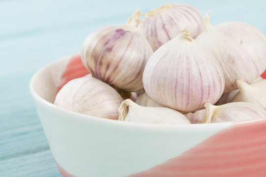 Garlic - A bunch of garlic bulbs in bowl a blue background.
