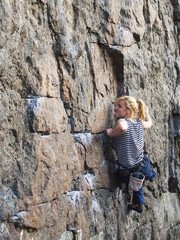 Young woman with rope climbs on the rock.
