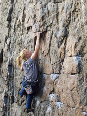 Young woman with rope climbs on the rock.