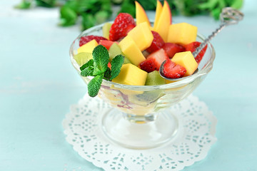 Fruit salad in glass bowl with mint on color wooden background
