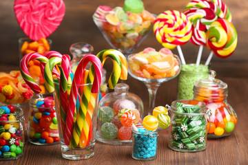 Colorful candies in jars on table on wooden background
