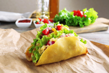 Tasty taco with vegetables on paper on table close up