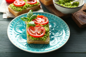 Vegan sandwich with avocado and vegetables on plate, on wooden background