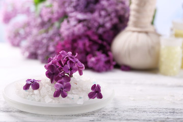 Sea salt, flowers and spa treatment on color wooden table, on light background