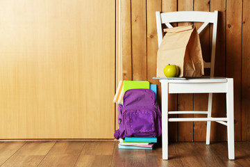 Backpack with school supplies on chair on wooden background