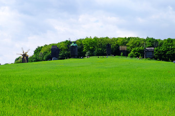 Obraz premium Old wooden windmills on green field, on blue sky background