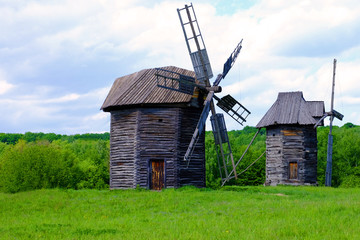Fototapeta na wymiar Old wooden windmills on green field, on blue sky background