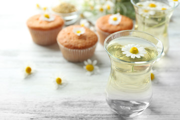 Fototapeta na wymiar Glass of chamomile tea with chamomile flowers and tasty muffins on color wooden background