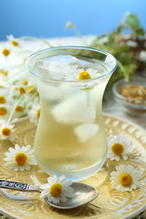 Obraz na płótnie Canvas Glass of cold chamomile tea with ice cubes and chamomile flowers on table, on colorful background