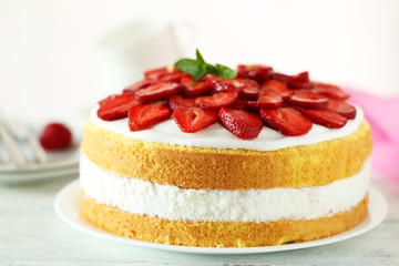 Sweet cake with strawberries on plate on white wooden background