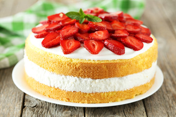 Sweet cake with strawberries on plate on grey wooden background
