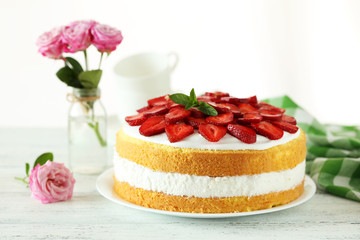 Sweet cake with strawberries on plate on white wooden background