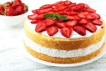 Sweet cake with strawberries on plate on white wooden background