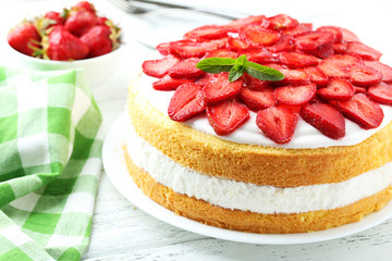 Sweet cake with strawberries on plate on white wooden background
