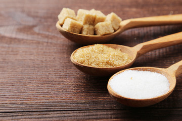 Various kinds of sugar in spoons on brown wooden background