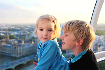 Family with young children enjoying trip to UK. Kids looking through the window of London Eye wheel. Beautiful view on London's southern part: cityscape, Westminster Abbey, Big Ben and Thames river - obrazy, fototapety, plakaty