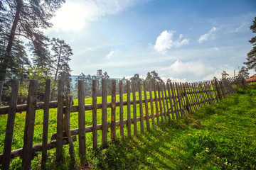 Fototapeta na wymiar Fence in the green field under blue cloud sky