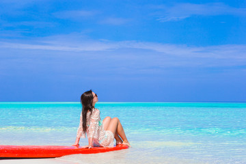 Young surfer woman at white beach on red surfboard