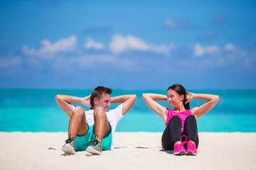 Fototapeta na wymiar Young fitness couple doing sit ups on white beach 