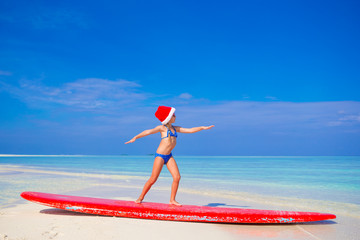Adorable little girl in Santa hat practice surfing position on