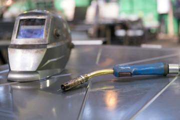 Welding equipment - protective mask and welding  torch at manufacture workshop workplace - obrazy, fototapety, plakaty