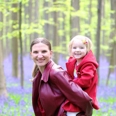 Fototapeta premium Mother and child outdoors. Happy family of two, young smiling woman and her cute toddler daughter enjoying beautiful day in the forest with bluebells