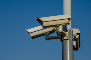 Three cctv camera on metal light pole, blue sky background