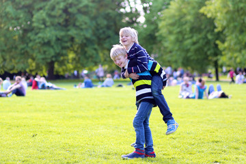 Happy kids playing in the park on beautiful summer sunny day. Two school boys, twin brothers, jumping and running together in Hyde park, London, UK. Brotherhood and friendship concept.