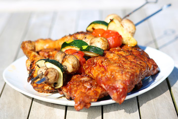 Assorted delicious grilled meat with vegetables on white plate on picnic table for family bbq party