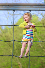 Adorable happy little child, blond sportive toddler girl, having fun outdoors climbing on playground in the park on a sunny spring or summer day