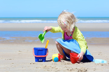 Happy little child on the beach. Cute toddler girl enjoying summer vacation at the North sea building sand castles and playing with plastic toys.
