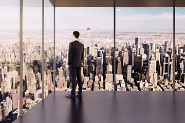 Businessman in empty office stands at the windows