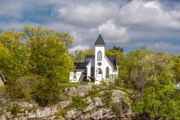  gorgeous amazing view of old vintage white church standing on a rock cliff in woods against blue cloudy sky background 