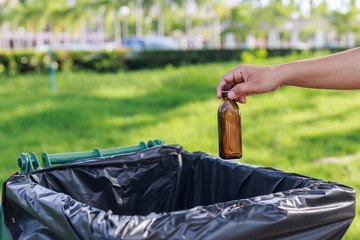 Hand throwing empty glass bottle into the trash