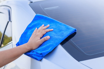 Woman hand with blue microfiber cloth cleaning the car