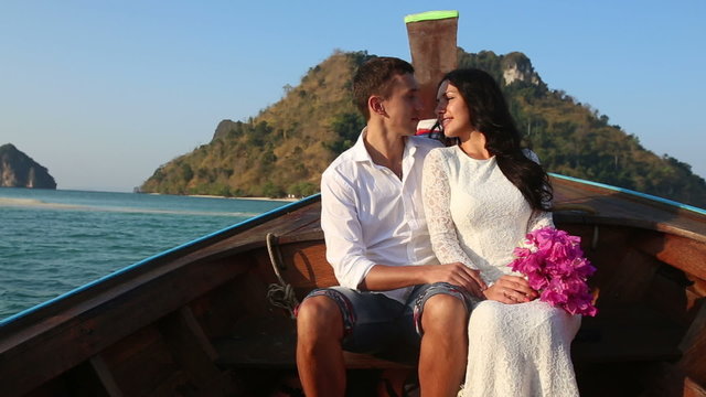bride and groom float in longtail boat to island at sunrise