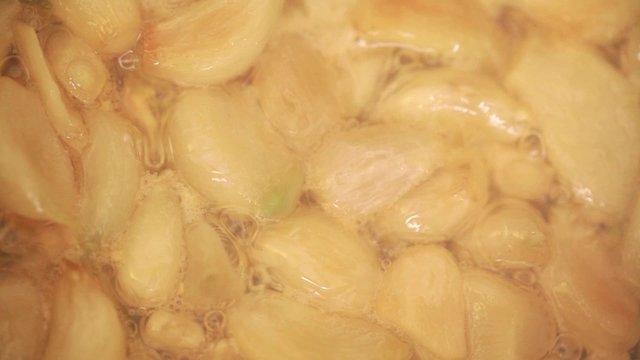 Garlic cloves cooking in deep cooking oil in frying pan; closeup